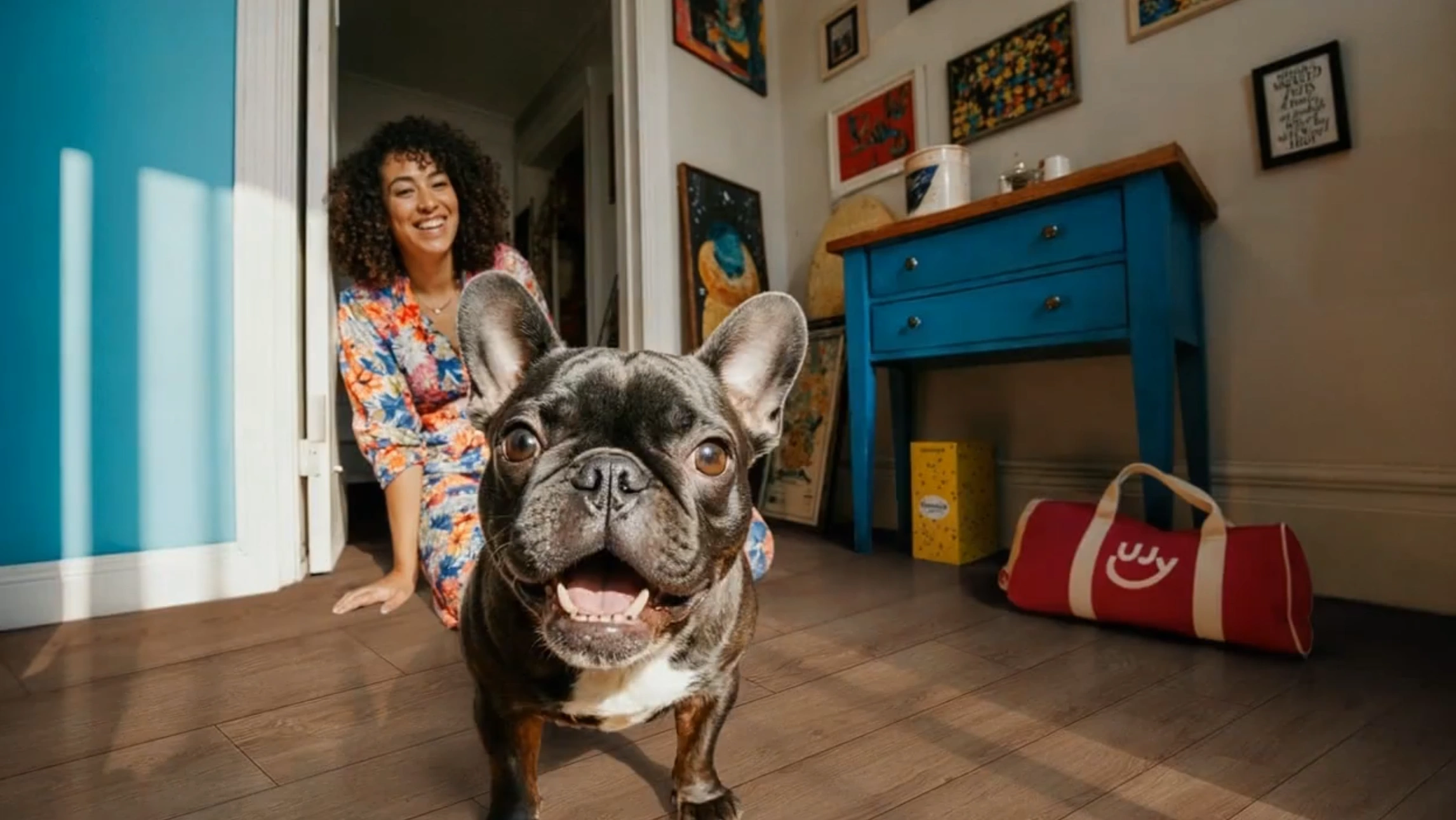 Ein Hund schaut in die Kamera, während eine Frau dahinter lächelt.